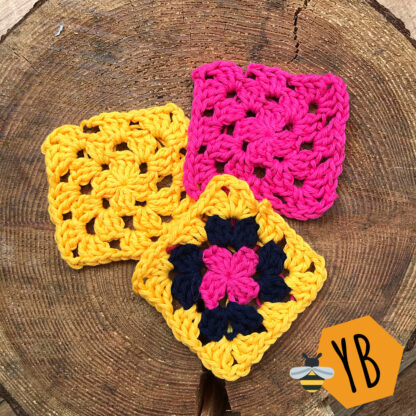 Three simple granny squares on a log slice, one fuchsia pink, one bright yellow, one with three layers of colour, fuchsia, navy and yellow.